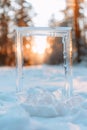 Ice frame stands in snow with light refracting through it. The sun sets behind trees, creating a warm glow in the cold winter Royalty Free Stock Photo