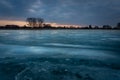 Ice on a frozen lake, trees on the horizon and dark cloud on the sky Royalty Free Stock Photo