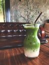 Ice green tea milk in glass on the wooden table with brown armchair background Royalty Free Stock Photo