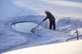 Ice hole in the lake in winter is equipped with a ladder for launching. Man cleans ice hole