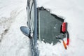 Ice scraper and brush for clearing automobile is on the hood of the car. Snow removing from car after blizzard. Partially cleaned