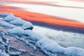 Ice on the shore of lake. Sky with pink clouds reflected in the cold water at sunset Royalty Free Stock Photo