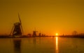 Ice skater silhouette on a frozen windmill canal at sunrise moment