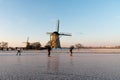 Ice skaters on a frozen windmill canal at sunrise moment