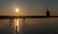 Ice skaters on a frozen windmill canal at sunrise moment