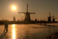 Ice skaters on a frozen windmill canal at sunrise moment Royalty Free Stock Photo