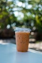 Ice Thai milk tea in a plastic cup on wooden table against a natural background Royalty Free Stock Photo