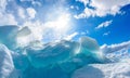 Iceberg in calm sea with blue sky, sun rays and clouds Royalty Free Stock Photo