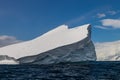 Iceberg in deep blue water. Coastline, Blue sky and clouds behind. Royalty Free Stock Photo