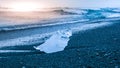 Icebergs sphashed by sea waves on black beach at sunrise time near Jokulsarlon glacier lake, Iceland