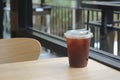 Iced black tasty coffee in plastic cup with straw on wooden table in coffee shop Royalty Free Stock Photo