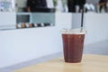 Iced black tasty coffee in plastic cup with straw on wooden table in coffee shop Royalty Free Stock Photo