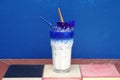 Iced Butterfly Pea Latte with milk and cinnamon stick on the wooden table.