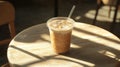 Iced Latte Coffee in a Clear Plastic Cup with Straw on a Wooden Table with Sunlight Shadows Royalty Free Stock Photo