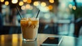 Iced Coffee with Cream and Ice in a Tall Glass with Straw, Near a Smartphone on Table Royalty Free Stock Photo