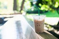 Iced coffee in a plastic cup with a straw placed on a wooden table surface blurred green background. Iced coffee with coffee straw Royalty Free Stock Photo