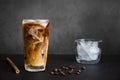 Iced coffee in tall glass with cream, container with ice, cocktail straw and coffee beans on dark background with copy space. Royalty Free Stock Photo