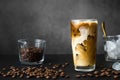 Iced coffee in tall glass with cream, container with ice and spoon, cocktail straw and coffee beans on dark background with copy Royalty Free Stock Photo