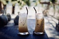 Iced cold coffee latte cappuccino summer refreshing drinks on wood table with blurred tropical palm trees beach background