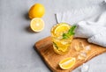 Iced drink with lemon, mint in a glass on a wooden board on a light background with citrus fruits