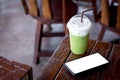 Iced green tea or matcha latte with milk foam in a plastic cup with brown straw and black mobile or smartphone and white scene on Royalty Free Stock Photo