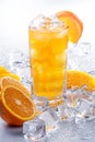 Iced orange juice in a glass with many condensation droplets, surrounded by ice cubes and slices of oranges