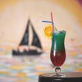 Iced summer cocktail. Cold drink on table. Two-layer red-green beverage in glass with orange slice and straw. Sailboat Royalty Free Stock Photo