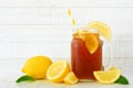 Iced tea in a mason jar glass with lemons, side view against white wood