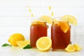 Iced tea in mason jar glasses with lemons, side view against white wood