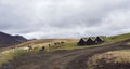 Icelandic traditional turf roof houses, group of icelandic horses and two farmer workers on dirt road in Southern Iceland