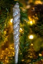 Icicle Christmas ornament in an artificial christmas tree with Christmas lights in background