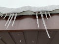 Icicles hang from the snow-covered roof. Frozen water on the roof in the cold. Cold winter near the house Royalty Free Stock Photo