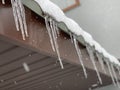 Icicles hang from the snow-covered roof. Frozen water on the roof in the cold. Cold winter near the house Royalty Free Stock Photo