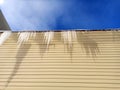 Icicles hanging from the roof against a blue sky and a beige wall Royalty Free Stock Photo