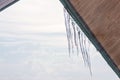 Icicles house roof against the blue white cloudy overcast sky