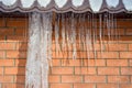 Icicles of ice hang from the edge of the roof against the red brick wall of the building. Background Royalty Free Stock Photo