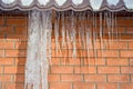 Icicles of ice hang from the edge of the roof against the red brick wall of the building. Background Royalty Free Stock Photo