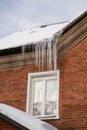Icicles over a window in a red brick wall of a residential building, brick winter background Royalty Free Stock Photo