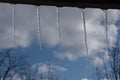 Icicles shimmering in the sun hanging from the roof against a blurred background of the cityscape, houses and trees.