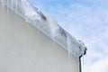 Icicles and snow falling from the roof. danger season winter. Blue sky with clouds on background.