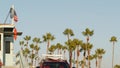 Iconic retro wooden lifeguard watch tower and baywatch red car. Life buoy, american state flag and palm trees against blue sky. Royalty Free Stock Photo