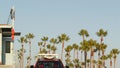 Iconic retro wooden lifeguard watch tower and baywatch red car. Life buoy, american state flag and palm trees against blue sky.