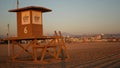 Iconic retro wooden orange lifeguard watch tower on sandy california pacific ocean beach illuminated by sunset rays. Private Royalty Free Stock Photo