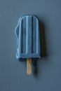 An icy blueberry popsicle melts over a simple blue background, deep blue hues and droplets capturing fleeting moments