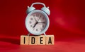 Idea word written on wooden block with alarm clock on red background.
