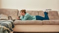 Ideal workplace. Young beautiful girl in casual clothes lying on the sofa in the living room and working on laptop Royalty Free Stock Photo