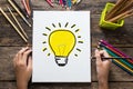 Ideas Concept , Hand of girl drawing a light bulb on paper and colorful pencils on wooden table Royalty Free Stock Photo