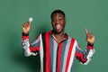 Emotional young african man, student holding bulb in his hand and looking at camera isolated on green studio background Royalty Free Stock Photo