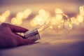 Ideas and innovation: Light bulb with LEDs is lying in the bed, hands touching. Spot lights in the blurry background