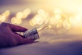 Ideas and innovation: Light bulb with LEDs is lying in the bed, hands touching. Spot lights in the blurry background